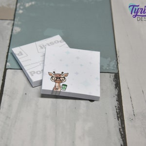 May include: A set of two white sticky note pads with a blue and white starry pattern. The top pad features a cartoon giraffe wearing glasses and holding a cup of coffee. The bottom pad has the word "Post-it" printed on it.