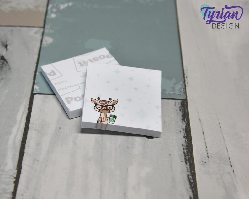 May include: A set of two white sticky note pads with a blue and white starry pattern. The top pad features a cartoon giraffe wearing glasses and holding a cup of coffee. The bottom pad has the word "Post-it" printed on it.