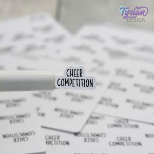 Könnte beinhalten: Weißer Aufkleber mit schwarzem Text, der "CHEER COMPETITION" lautet. Der Aufkleber befindet sich auf einem weißen Stift.