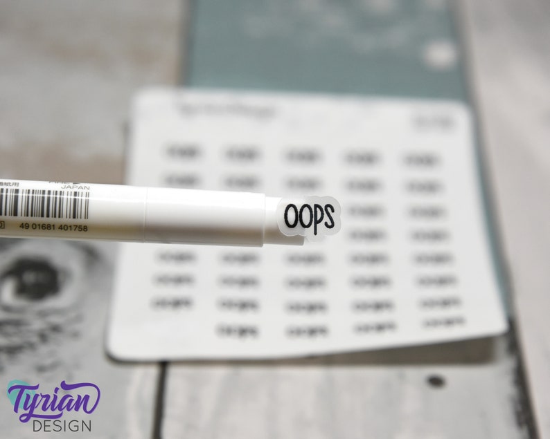 May include: A white marker pen with a black and white sticker that says "oops" on it. The sticker is round and has a white border.