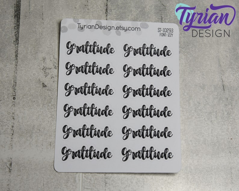 May include: A sheet of 10 clear stickers with the word "Gratitude" written in black cursive script. The stickers are arranged in two rows of five. The sheet is white with a black border.
