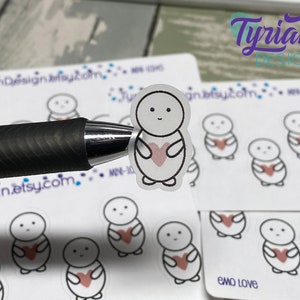 Puede incluir: Una hoja de pegatinas con un personaje de dibujos animados simple que sostiene un corazón. Las pegatinas son blancas con contornos negros y un corazón rosa. El texto "emo love" está impreso en la hoja.