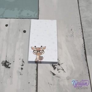 Op de afbeelding: Een wit notitieboekje met een schattige cartoon-giraf die een bril draagt en een kopje koffie vasthoudt. De achtergrond is lichtpaars met witte sterren.
