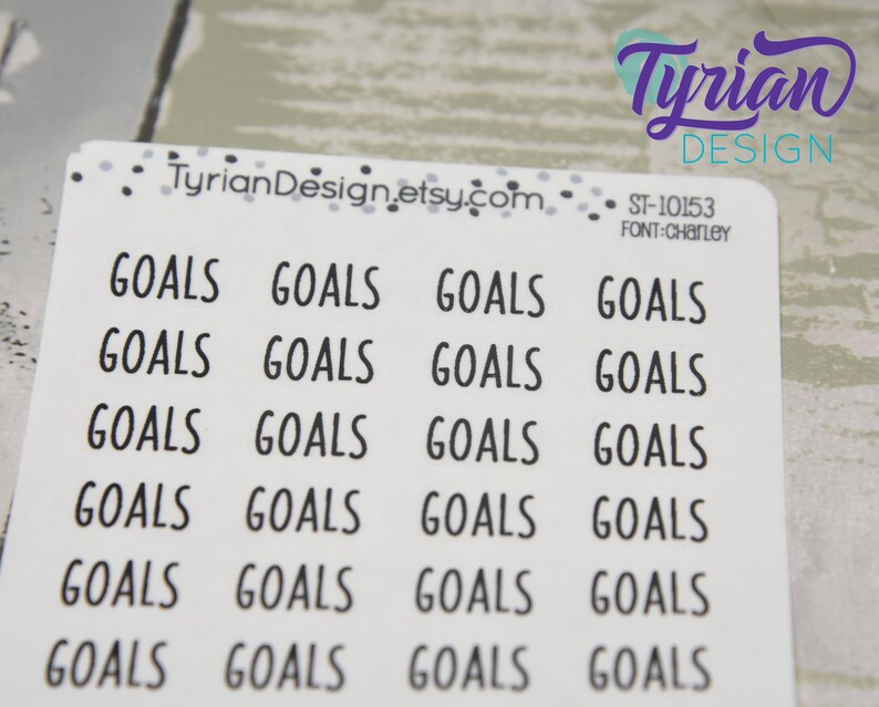May include: A sheet of white stickers with the word "GOALS" printed in a black, sans-serif font. The stickers are arranged in rows and columns. The top right corner has the text "Tyrian Design" in purple script.
