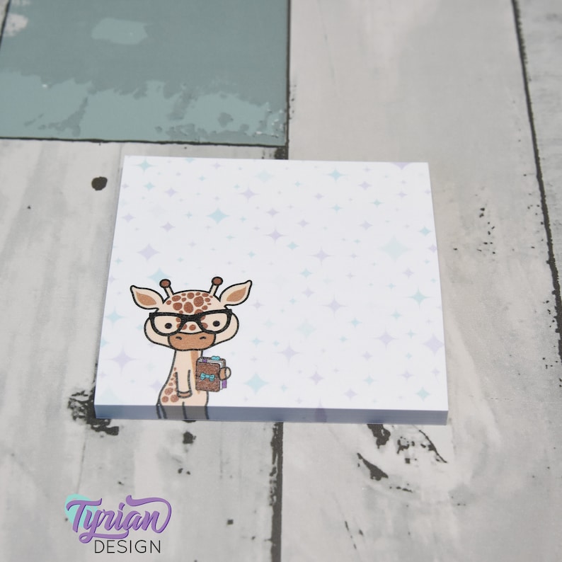 Op de afbeelding: Een wit notitieblok met een lichtpaarse en lichtblauwe glitterachtergrond. In het midden van het notitieblok staat een cartoon-giraffe met een bril die een boek vasthoudt.