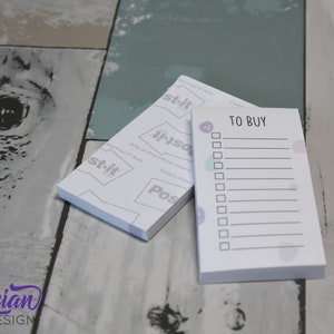 May include: A white notepad with a pink and purple watercolor design. The notepad has a checklist with the title "TO BUY" printed on the front.