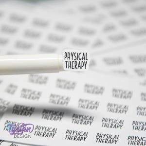 May include: A white sticker with the words "PHYSICAL THERAPY" in black, held by a white pen. The sticker has a rounded rectangular shape. Other stickers with the same text are in the background.