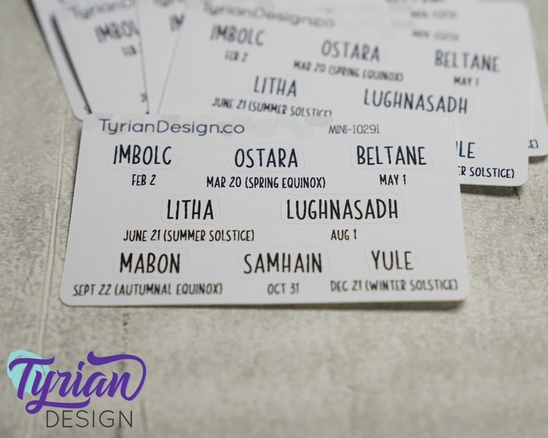 May include: A white card with the names of the eight pagan holidays, including Imbolc, Ostara, Beltane, Litha, Lughnasadh, Mabon, Samhain, and Yule, with their corresponding dates and descriptions.