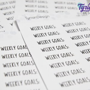 May include: A sheet of white paper with the text "Weekly Goals" repeated multiple times in black ink. The text is in a handwritten font.