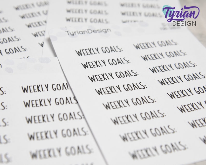 May include: A sheet of white paper with the text "Weekly Goals" repeated multiple times in black ink. The text is in a handwritten font.