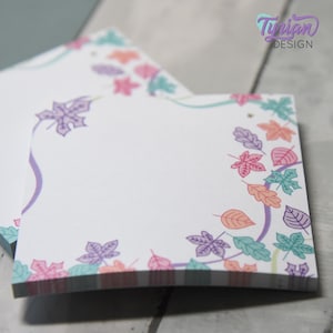 May include: White square notepads with a colorful leaf border in shades of purple, pink, orange, and teal. The notepad has a purple curved line design. The text "Tynian DESIGN" is in the upper right corner.