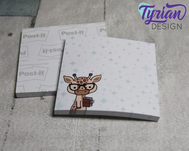 Op de afbeelding: Een stapel Post-it-briefjes met een schattige cartoon-giraf die een bril draagt en een boek vasthoudt. De achtergrond is lichtblauw met witte sterren.