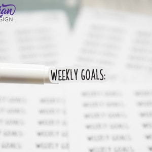 以下が含まれることがあります： 黒い文字で「WEEKLY GOALS:」と書かれた白いステッカー