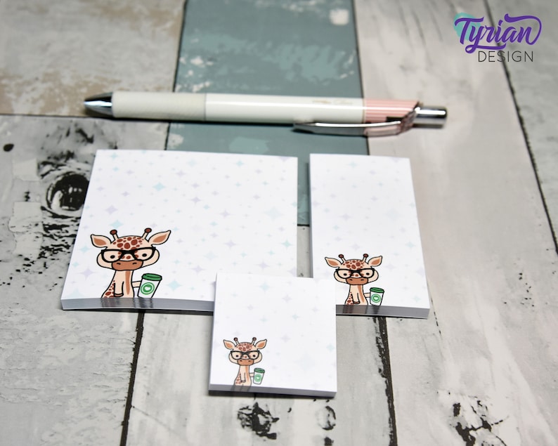 May include: Three different sizes of sticky note pads with a cute cartoon giraffe wearing glasses and holding a cup of coffee. The background of the note pads is white with a light blue and purple star pattern.