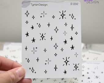 Könnte beinhalten: Ein Bogen weißer Aufkleber mit einem Muster aus schwarzen Sternen und Sternen. Der Text "TyrianDesign" und "ST-10542" ist auf dem Aufkleberbogen aufgedruckt. Die Aufkleber werden von einer Hand gehalten.
