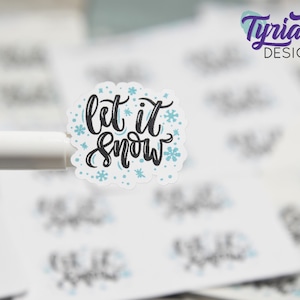Peut inclure: Autocollant blanc avec des flocons de neige bleus et une inscription noire qui dit "Let it snow".