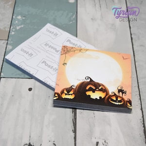 May include: Halloween-themed Post-it notes featuring a design of jack-o'-lanterns, a full moon, and a spider web. The notes are square-shaped and stacked, with the Post-it brand visible on the back of the pad. The design includes the text "Tynian DESIGN".