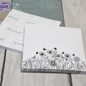 Può includere: Blocchi di Post-it bianchi con un design floreale in bianco e nero e dettagli di farfalle. I blocchi hanno un bordo a righe grigie nella parte inferiore. Il logo "Tyrian Design" è visibile. I Post-it sono impilati. Dimensioni: circa 7,6 cm.