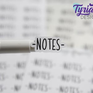 May include: A white marker pen with a clear sticker attached to the end. The sticker has the word "NOTES" written in black.