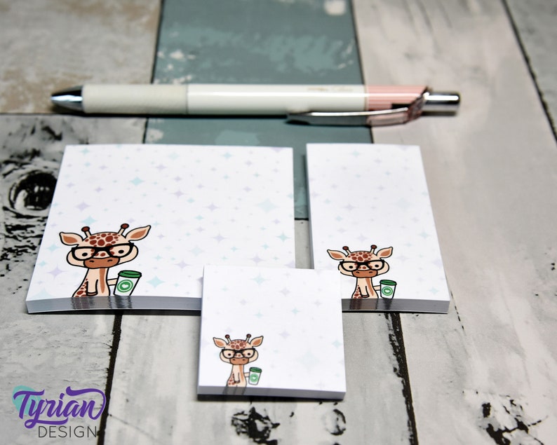 May include: Three different sizes of sticky note pads with a cartoon giraffe wearing glasses and holding a cup of coffee. The background of the note pads is white with a light blue and purple star pattern.