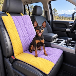 Peut inclure: Une housse de siège auto matelassée présentant un design color-block en jaune vif et lavande doux. Le tapis de protection rectangulaire est fixé au siège de véhicule en cuir noir et offre une surface pour qu'un petit chien noir et feu s'assoie.