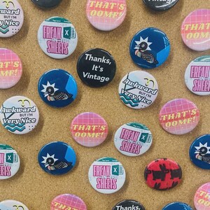May include: A collection of circular pin-back buttons featuring various designs including text that reads "THAT'S OOMF", "FREAK IN THE SHEETS", "Thanks, It's Vintage", and "Awkward BUT I'M VERY NICE", alongside illustrations of a bird and a rabbit.