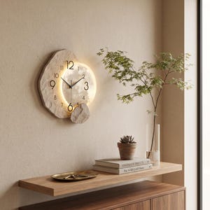 May include: A wall clock with a textured, stone-like beige frame and a circular, illuminated centre face. The clock features black numerals and thin black hands, with a warm light glowing from behind the circular face, mounted on a wall.