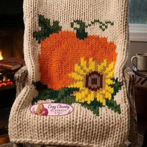 Könnte beinhalten: Eine cremefarbene, grob gestrickte Decke mit einem großen orangefarbenen Kürbis und einer gelben Sonnenblume mit grünen Blättern. Ein rosa ovales Logo zeigt den Text Cozy Chunky BLANKETS by Sharon mit einer Illustration.