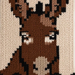 May include: A chunky knit blanket featuring a pixelated donkey portrait in shades of brown, black, and cream. The design displays a donkey head with long ears and a light-colored muzzle. A logo in the bottom right corner reads Cozy Chunky BLANKETS by Sharon.