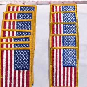 May include: A collection of rectangular embroidered patches featuring the American flag with red, white, and blue stitching and a gold border. A measuring tape is visible at the top, showing the patches are approximately 3.5 inches in width.