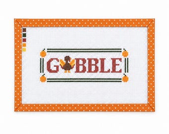 Op de afbeelding: Een rechthoekig kruissteekpatroon op witte stof met de tekst GOBBLE in rode letters, waarbij een bruine kalkoen de letter O vervangt. Het ontwerp is omlijst door een oranje rand met witte stippen en bevat een legenda voor de kleuren.
