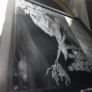 May include: A black framed wall art piece featuring a high-contrast white graphic illustration on a black background. The artwork depicts a stylized, elongated figure with branch-like appendages and intricate, flowing white line work throughout.