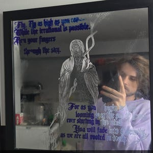 May include: A square wall mirror with a black frame featuring a white line-art illustration of a hooded figure and purple gothic-style text that reads: Fly, Fly as high as you can, While the irrational is possible, Run your fingers through the sky.