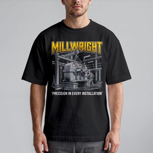 May include: A black t-shirt featuring a graphic illustration of a millwright working on industrial machinery in a factory setting. The text MILLWRIGHT appears in yellow above the image, and the text PRECISION IN EVERY INSTALLATION appears below.