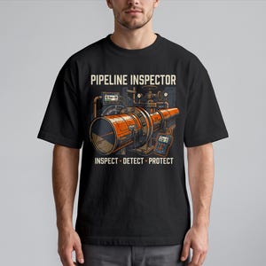 Może przedstawiać: Czarny t-shirt z grafiką przedstawiającą pomarańczowy rurociąg przemysłowy z manometrami i sprzętem pomiarowym. Nad grafiką znajduje się napis PIPELINE INSPECTOR, a pod grafiką napis INSPECT - DETECT - PROTECT.