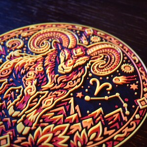 Puede incluir: Un posavasos circular con un dise&ntilde;o en relieve de varias capas que muestra un carnero con grandes cuernos curvados. La ilustraci&oacute;n utiliza una paleta de colores vibrantes en amarillo, naranja y rojo sobre un fondo oscuro con estrellas.