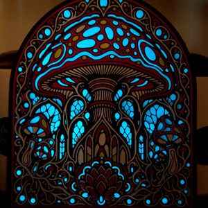 May include: An arched wall art piece featuring a layered design of mushrooms and intricate patterns. The artwork displays a dark frame with cutouts that reveal a vibrant, glowing cyan light behind the red and black detailed mushroom motifs.