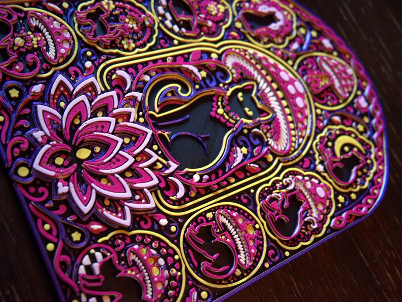 Pu&ograve; includere: Un'opera d'arte in legno tagliata al laser a pi&ugrave; strati con motivi intricati in tonalit&agrave; vivaci di magenta, viola, giallo e nero. Il design include gatti stilizzati, funghi e un grande fiore di loto, il tutto disposto in una composizione complessa e simmetrica con un profondo rilievo dimensionale.