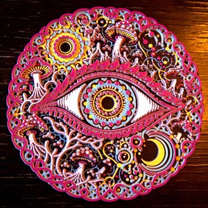 May include: A circular multi-layered wall art piece featuring a central eye motif surrounded by intricate patterns of mushrooms, a crescent moon, and sun-like shapes in vibrant shades of hot pink, bright yellow, light blue, and deep black.