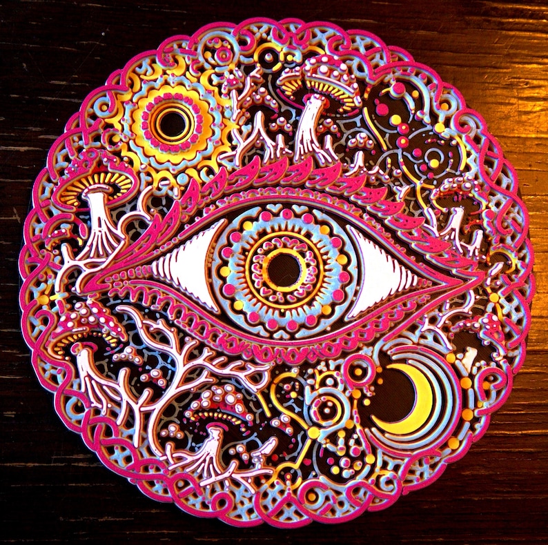 May include: A circular multi-layered wall art piece featuring a central eye motif surrounded by intricate patterns of mushrooms, a crescent moon, and sun-like shapes in vibrant shades of hot pink, bright yellow, light blue, and deep black.
