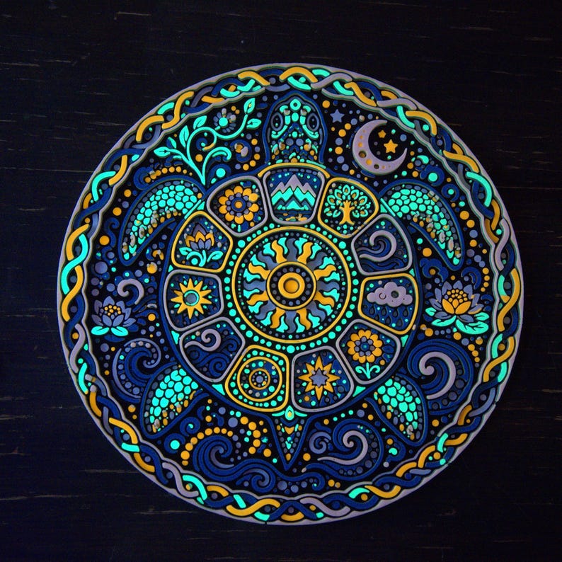 May include: A circular wall art piece featuring a central sea turtle with a shell divided into segments containing sun, mountain, tree, and floral motifs. The design uses a vibrant palette of glowing blue, yellow, and purple against a dark background.
