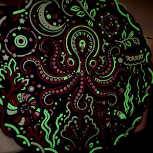 Peut inclure: Une plaque d&eacute;corative circulaire repr&eacute;sentant une pieuvre centrale entour&eacute;e de motifs marins complexes, notamment un croissant de lune, des coquillages, des algues et du corail. Le design m&ecirc;le des tons rouge fonc&eacute; et noir avec des accents vert clair.