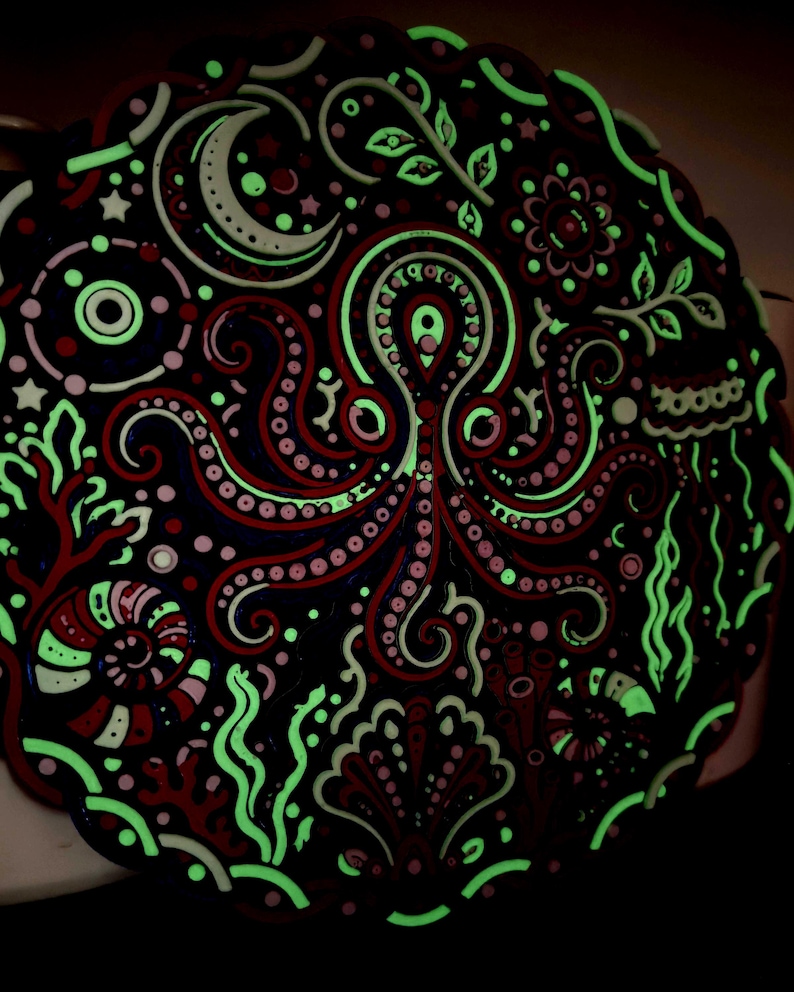 Peut inclure: Une plaque d&eacute;corative circulaire repr&eacute;sentant une pieuvre centrale entour&eacute;e de motifs marins complexes, notamment un croissant de lune, des coquillages, des algues et du corail. Le design m&ecirc;le des tons rouge fonc&eacute; et noir avec des accents vert clair.