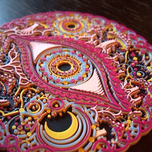 May include: A circular, multi-layered wall art piece featuring an intricate eye design at the center. The artwork is composed of stacked, laser-cut elements in vibrant shades of hot pink, bright yellow, light blue, and orange against a black base.