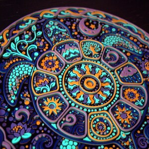 May include: A circular multi-layered wooden wall art piece featuring a stylized sea turtle. The design incorporates intricate patterns of suns, moons, flowers, and mountains in vibrant shades of neon blue, purple, orange, and dark navy blue.