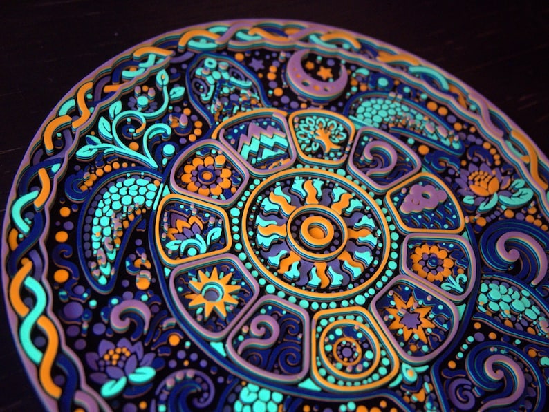 May include: A circular multi-layered wooden wall art piece featuring a stylized sea turtle. The design incorporates intricate patterns of suns, moons, flowers, and mountains in vibrant shades of neon blue, purple, orange, and dark navy blue.