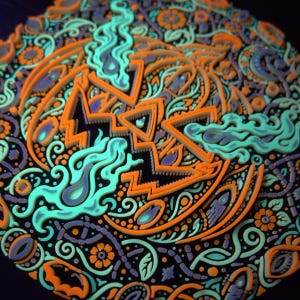 Close active-UV detail of the raised jack-o’-lantern face and surrounding Halloween ornament.