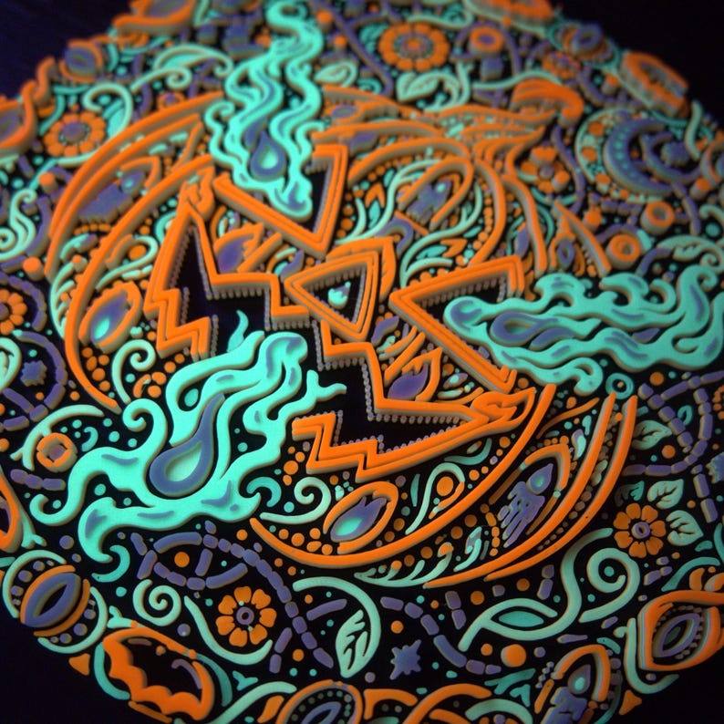 Close active-UV detail of the raised jack-o’-lantern face and surrounding Halloween ornament.