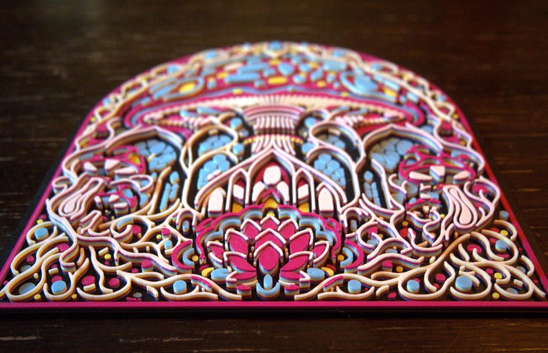 May include: A multi-layered, arched wall art piece featuring intricate, laser-cut designs in vibrant shades of magenta, light blue, yellow, and white. The composition displays a central lotus-like floral motif surrounded by swirling, organic patterns.