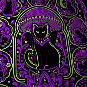 Pu&ograve; includere: Una spilla in metallo nero con la sagoma centrale di un gatto sotto un fungo, circondata da motivi pi&ugrave; piccoli di gatti e funghi. Il design &egrave; accentuato da smalto verde neon e viola, creando un aspetto luminoso ad alto contrasto.